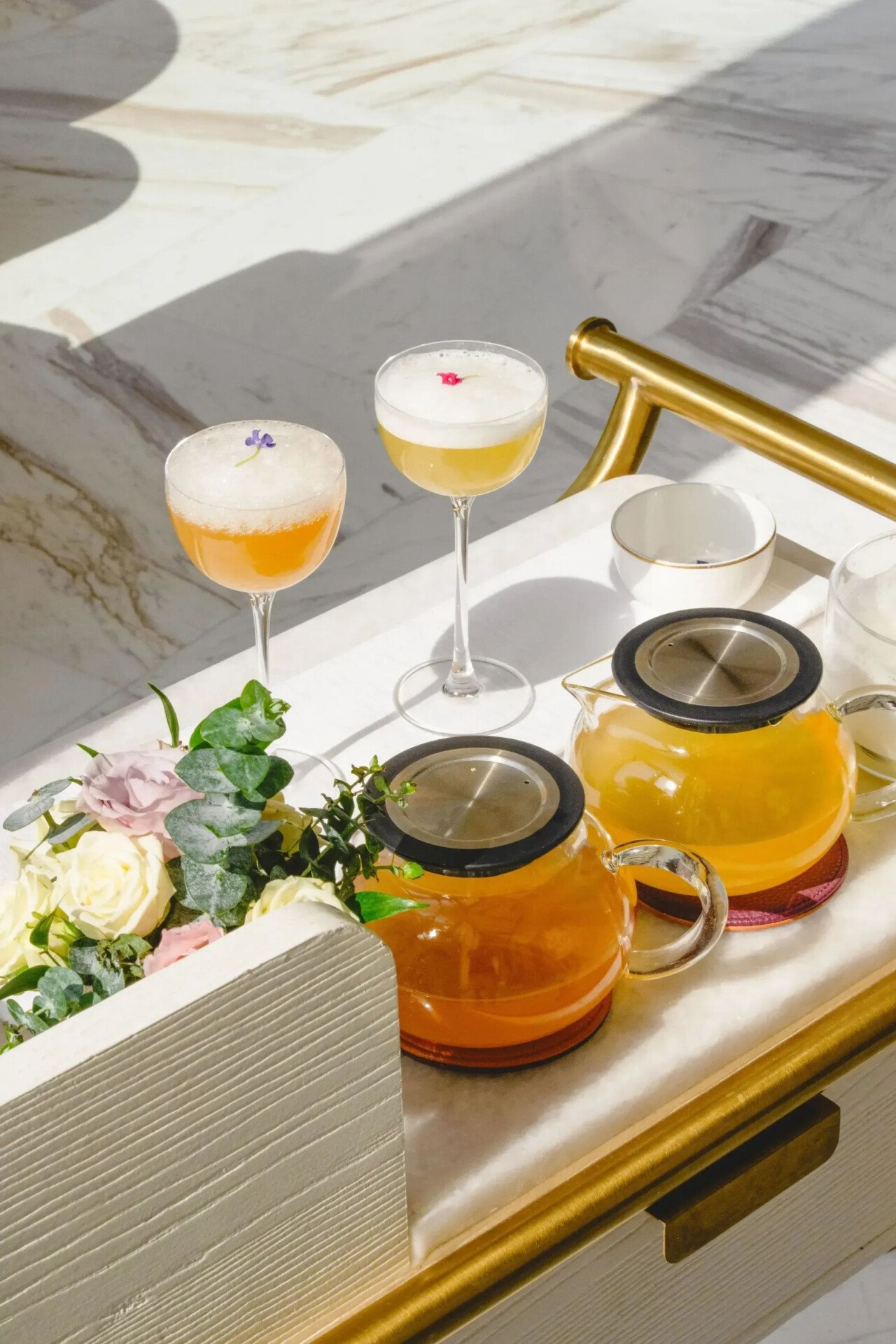 Summer Afternoon Tea at The Gallery located at The Lana, Dorchester Collection, Dubai. Including bites and beverage offerings. The afternoon tea is served in the lobby, on a table dressed with a white cloth against soft shadows. 