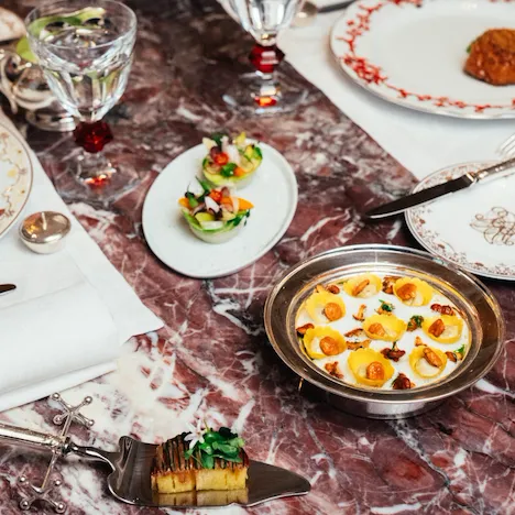 Table setting with dishes, glasses, cutlery, and decorated plates on a marble surface.