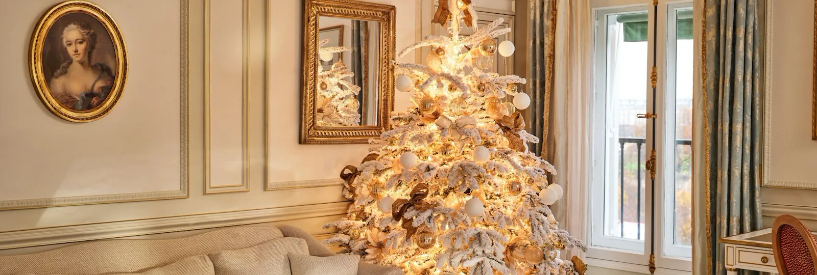Large view of a Prestige Suite with a table and a couch next to a Christmas Tree with decorations and artificial snow on it, at Le Meurice, Paris
