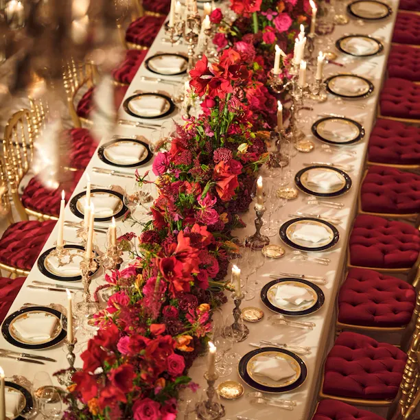 Dinner set up with a long table and red flowers captured in Le Salon Haute Couture, at Hôtel Plaza Athénée, Paris - Dorchester Collection.