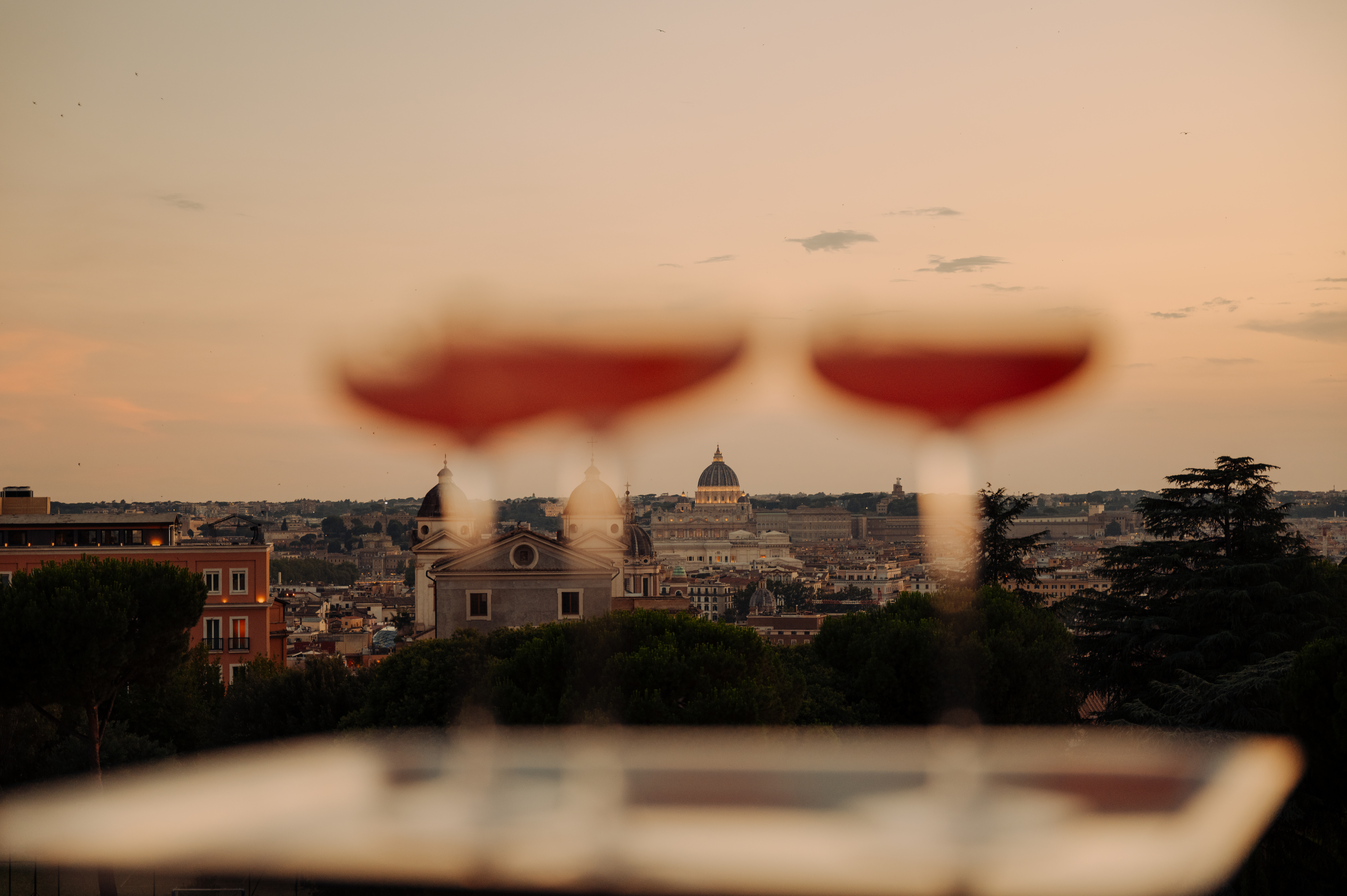 cocktails on a tray held up against a cityscape sunset view with a dome and clouds in the background