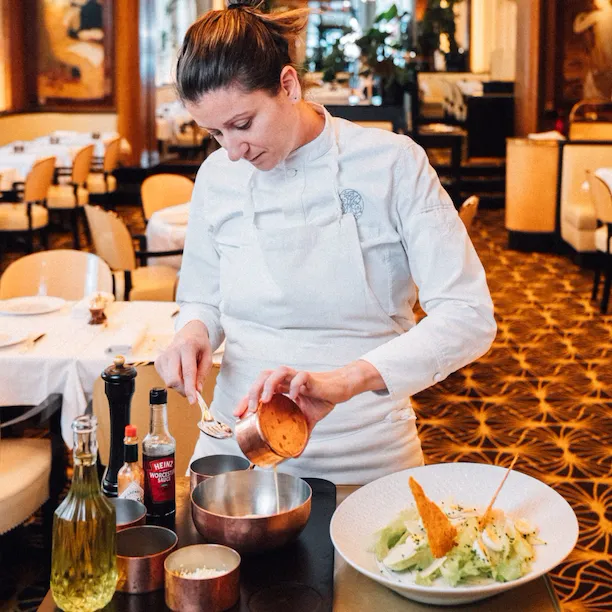 Person in chef's uniform preparing a dish in a restaurant kitchen setting.