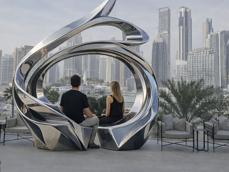 a couple sitting on the JD Malat installation in front of The Lana, enjoying Burj Khalifa