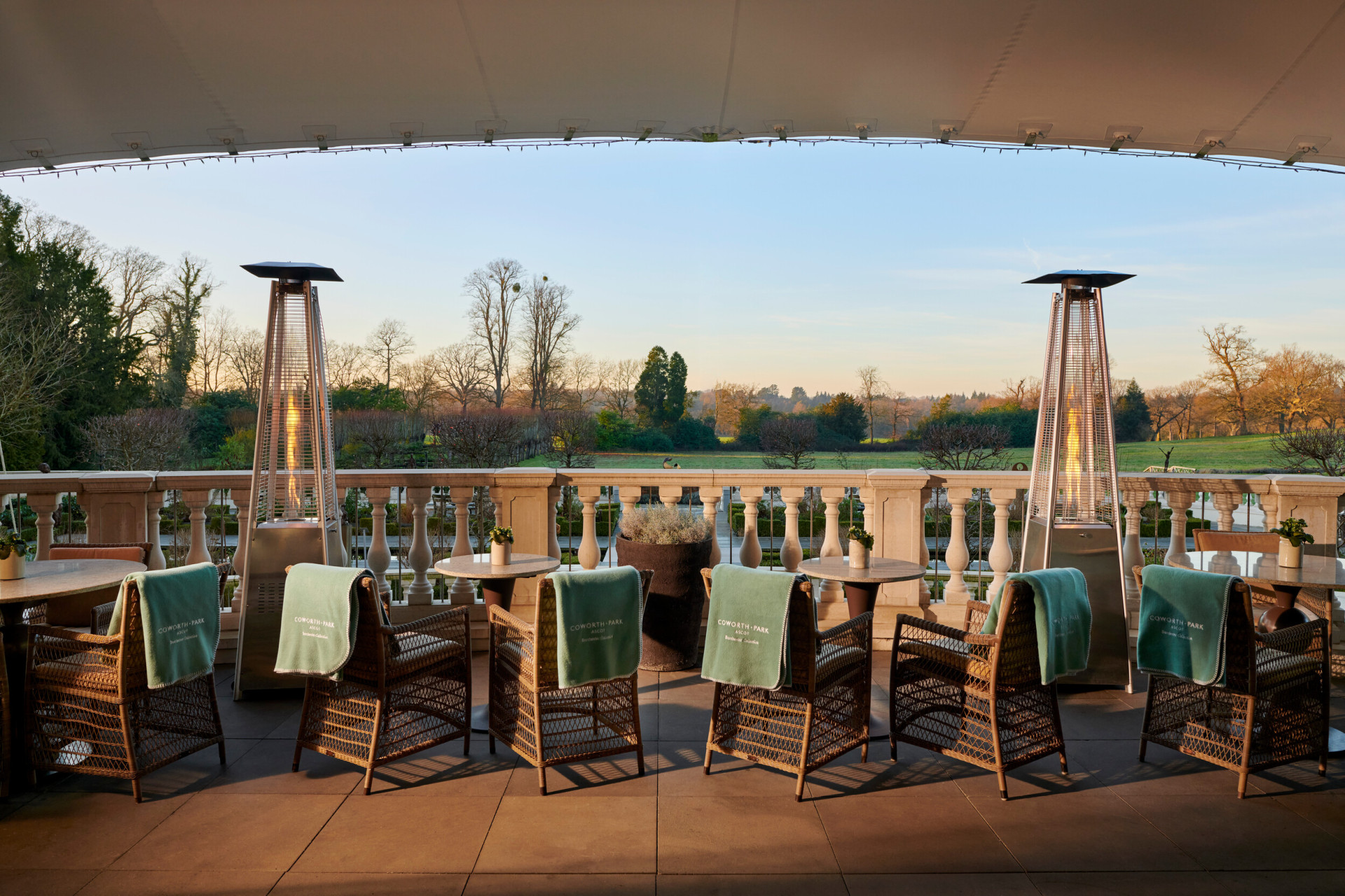 Drawing room terrace overlooking meadow at sunset with heaters, blankets and tables 