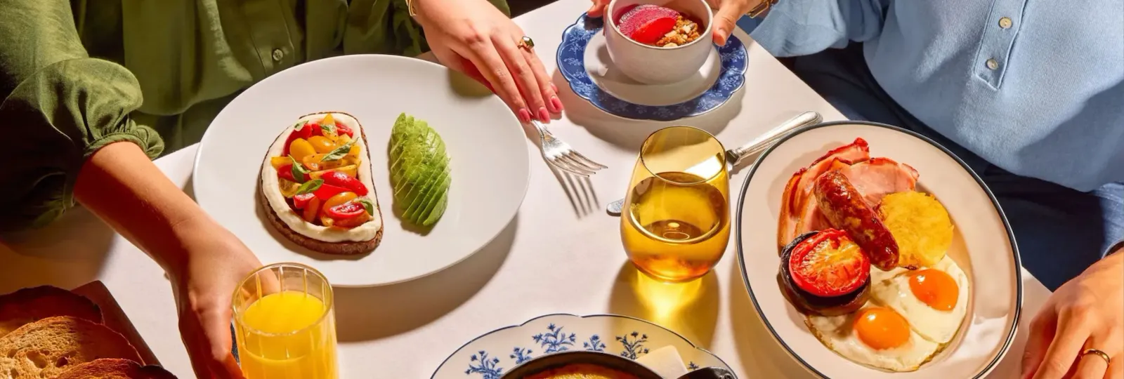 Dining table at The Grill at The Dorchester, showcasing a selection of breakfast and brunch dishes including tomato on toast with basil, eggs and bacon, a baked gratin-style dish, fresh berries and glasses of orange juice.