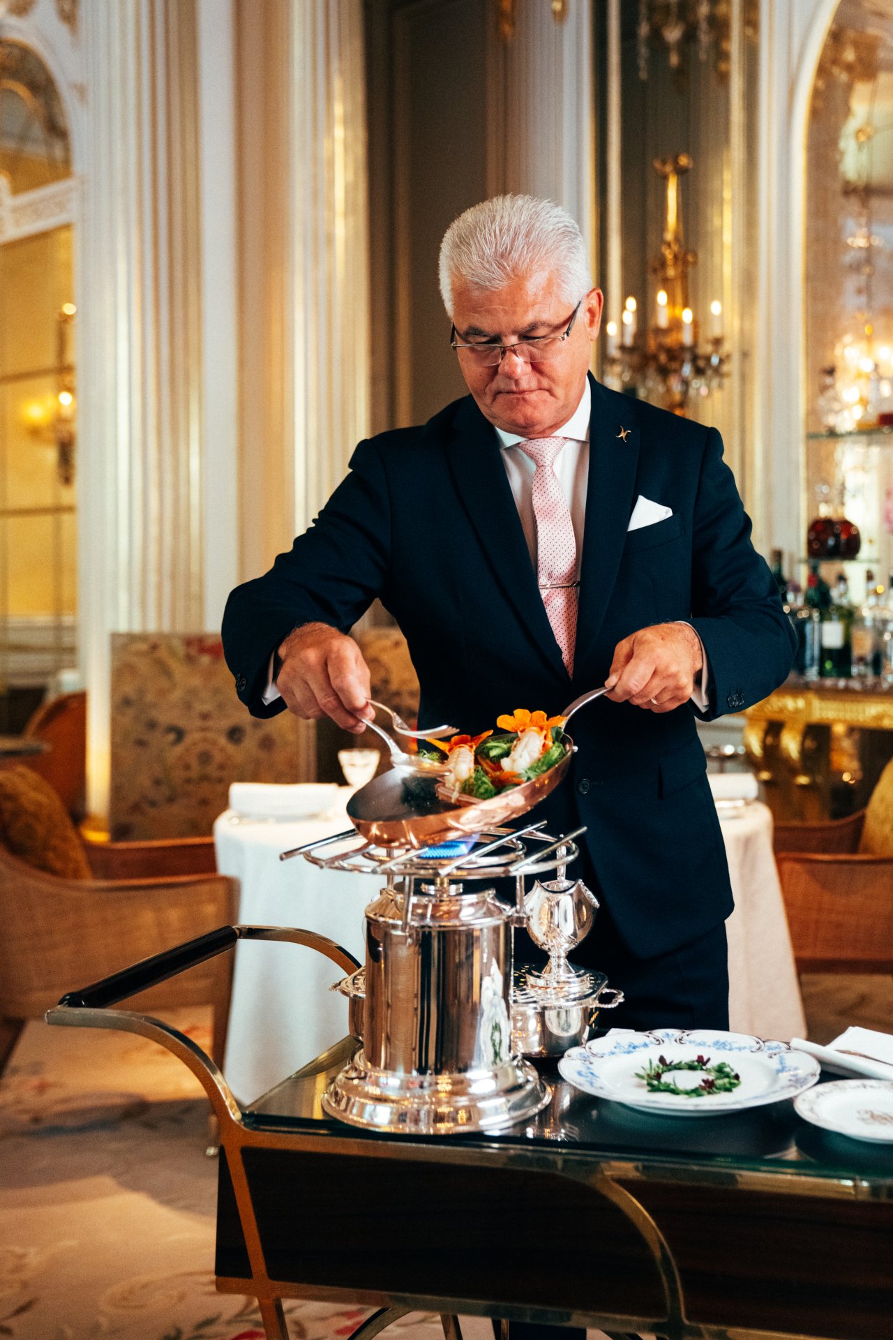 Person serving food with tongs in a luxurious dining room, elegant and focused.