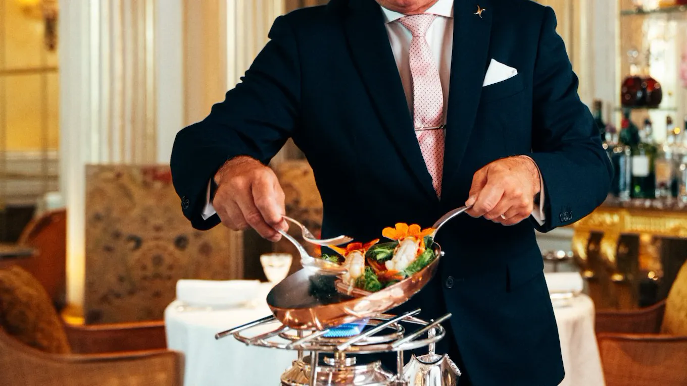 Person serving food with tongs in a luxurious dining room, elegant and focused.