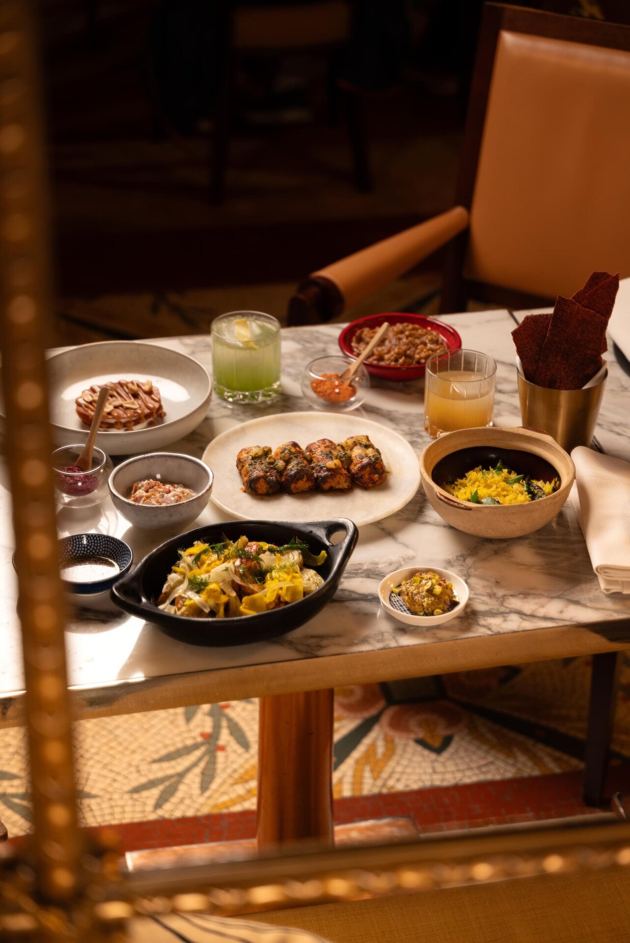On the marble table we can see various colorful dishes, arranged for the jiwan pop-up. Cocktails are also on the table.  In the background, we can see the armchair behind the table at Le Meurice, Paris.