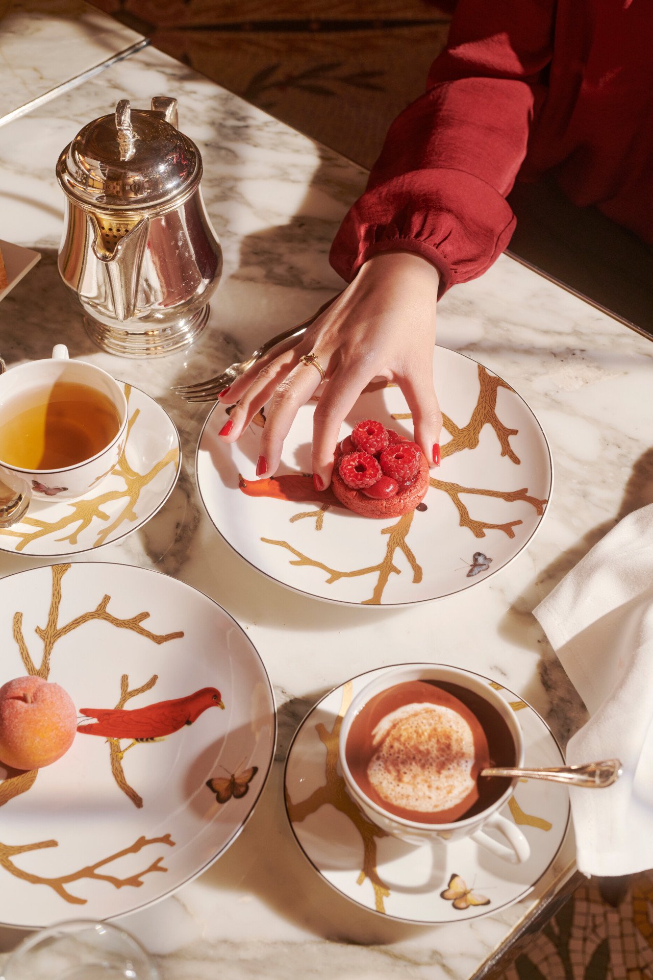 Some details of the tea time with a hand taking a raspberry cookie of Cédric Grolet next to hot drinks and a peach, at Le Meurice, Paris  
